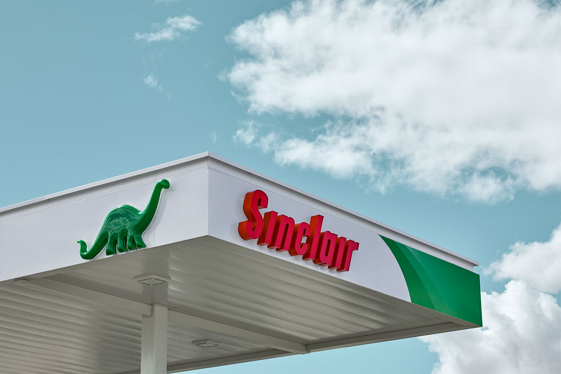 A wide Sinclair gas station awning extends into a background of blue sky and white clouds