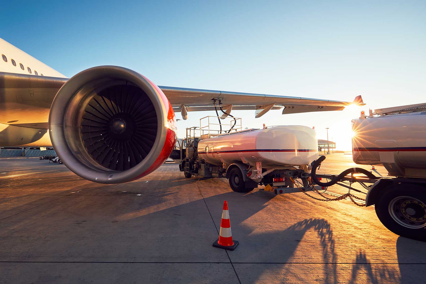 A commercial airplane is being refueled on the tarmac, with a fuel truck connected to the wing.